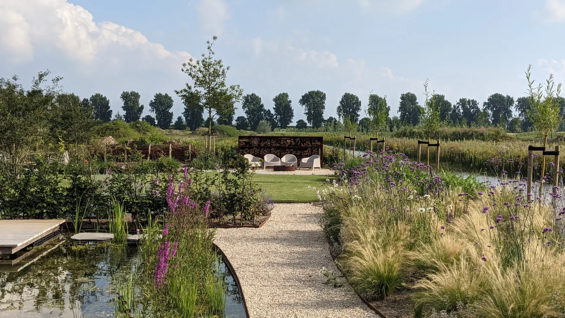 Een gebogen grindpad loopt door siergrassen en paars bloeiende planten.