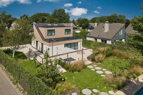Luchtbeeld van een woning met terrassen, gazon, stapstenen en beplante borders.