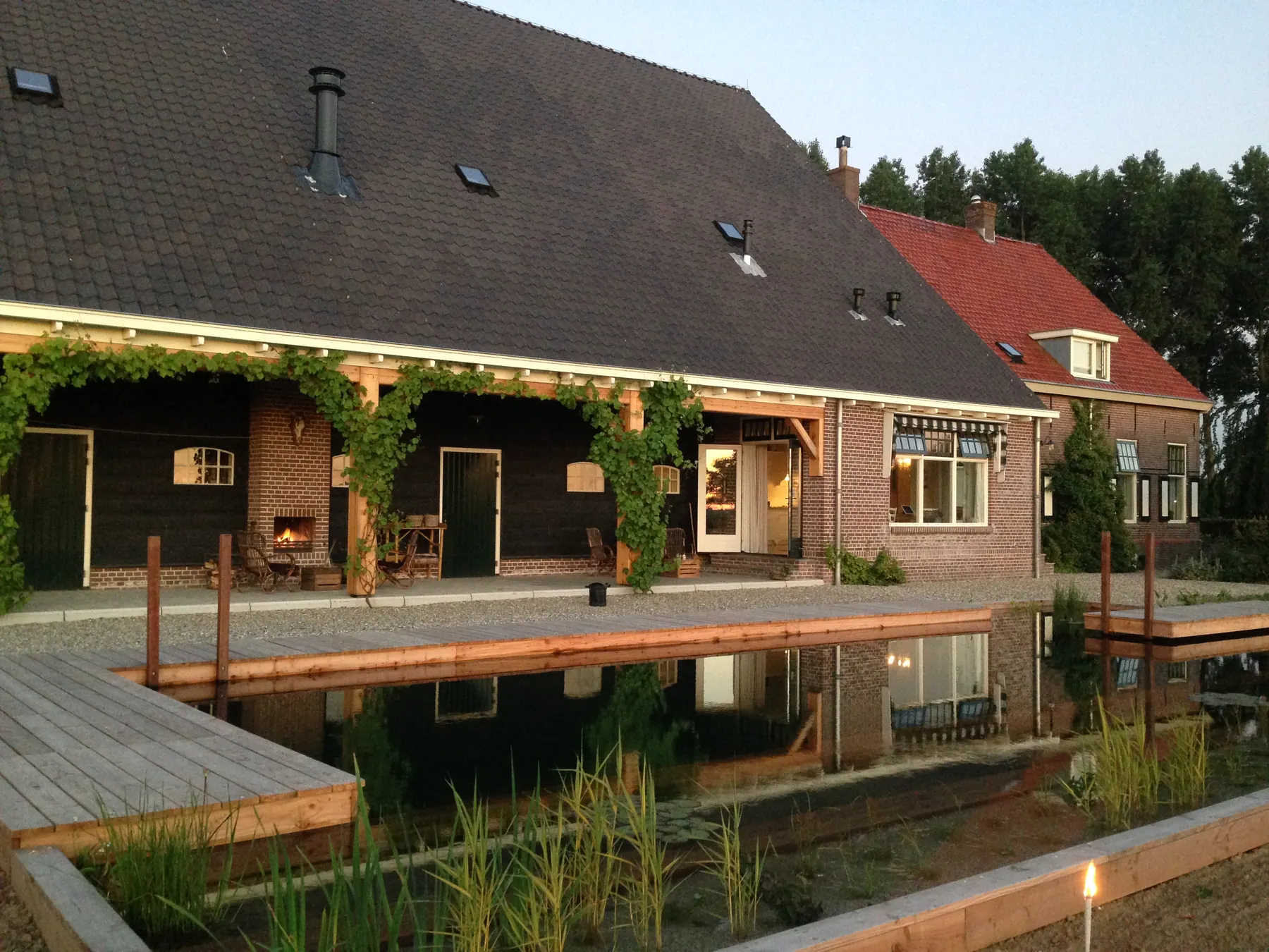 Een langgerekte vijver weerspiegelt een woonboerderij en de avondlucht.